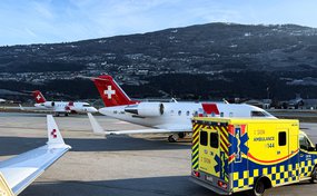 Ambulance vehicle parked on the apron in front of a Rega ambulance jet with Swiss cross at an alpine airport.