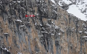 Drei Personen hängen unterhalb des Helikopters am Seil der Rettungswinde