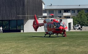 Un hélicoptère de sauvetage Rega Airbus H145 est posé sur une pelouse devant un bâtiment, avec sa porte ouverte.