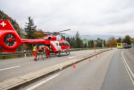 Zum Downloadformular für das Bild Rega-Helikopter auf einer gesperrten Strasse, Crew beim Einladen in den Rettungshelikopter.