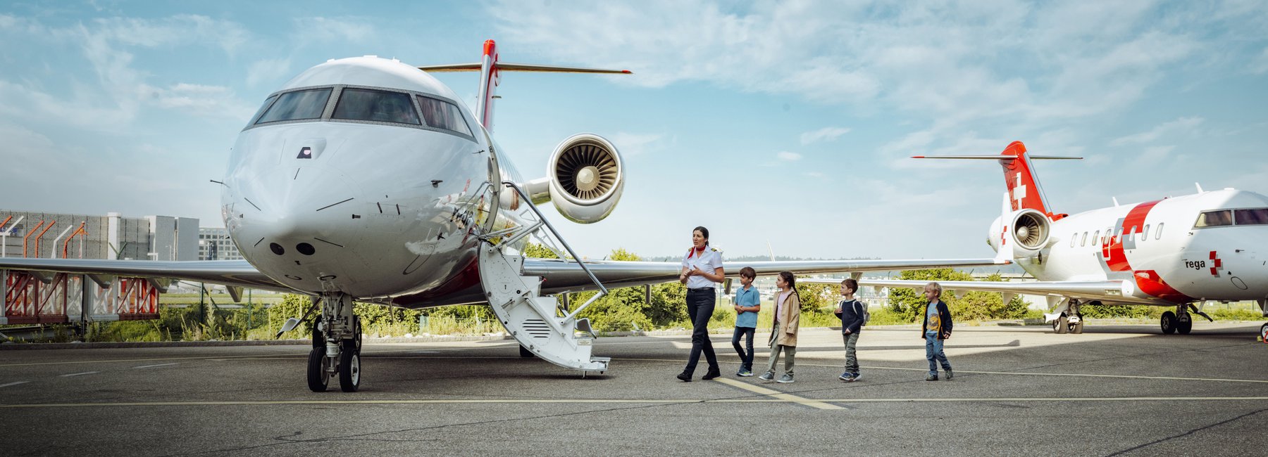 Eine Rega-Mitarbeiterin geht mit einer Gruppe von Kindern auf dem Rollfeld an einem Ambulanzjet vorbei.