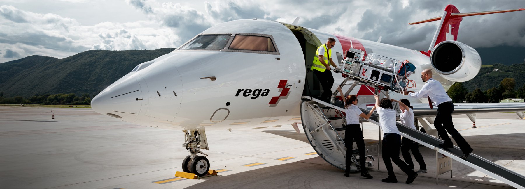 Rega-Mitarbeitende laden medizinisches Gerät in einen Ambulanzjet auf einem Rollfeld.