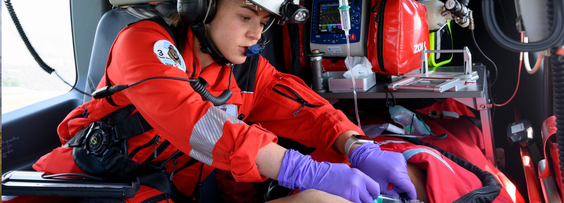 Eine Rega-Ärztin oder ein Rega-Rettungssanitäter in Uniform und mit Handschuhen behandelt einen Patienten im Inneren eines Helikopters.