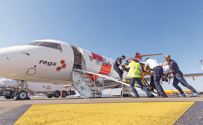 Mehrere Rega-Mitarbeitende verladen einen Patienten auf einer Trage über die Treppe in den Ambulanzjet der Rega, der auf dem Rollfeld steht.