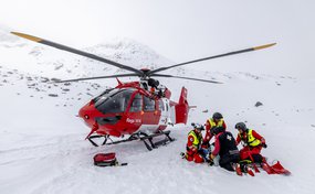 Rega-Crew versorgt einen Patienten im Schnee neben einem Rettungshelikopter im Hochgebirge.