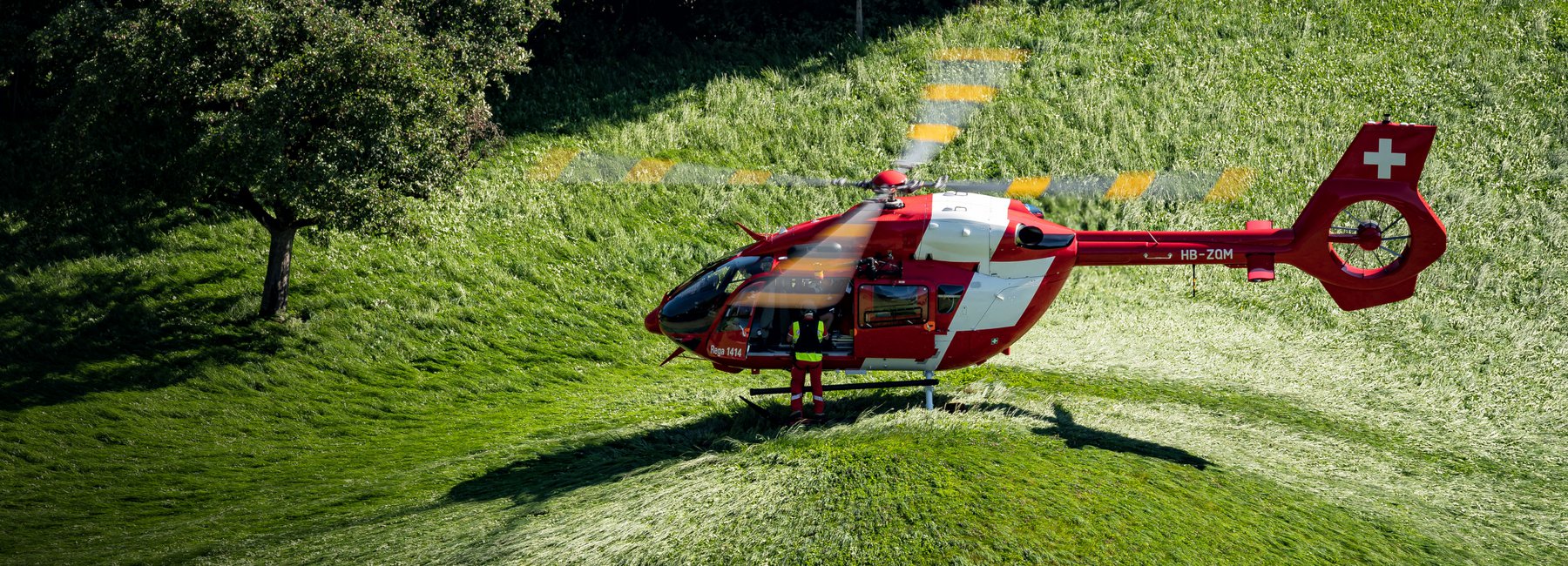 A Rega helicopter is parked on a green meadow with tall grass.